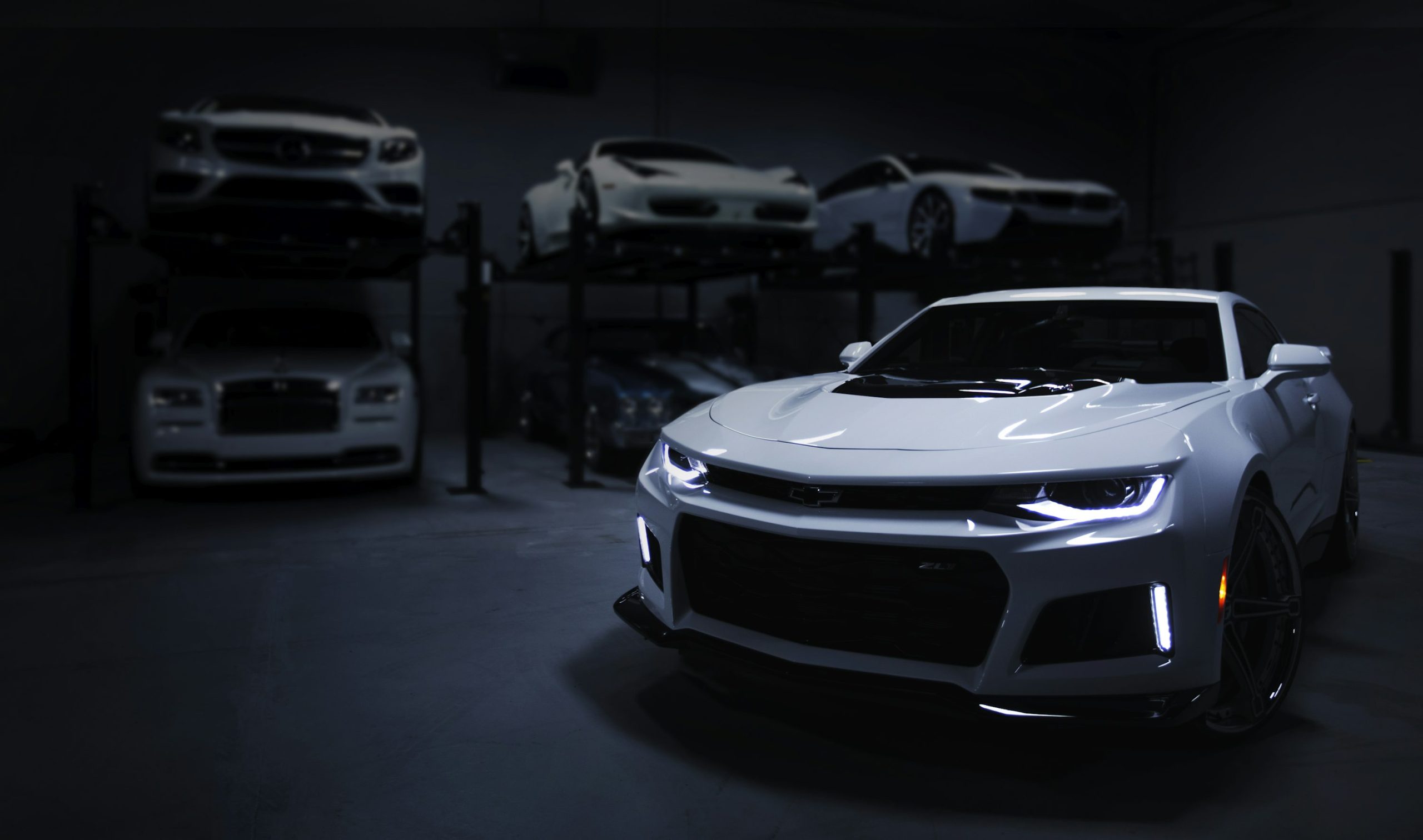 A white performance car with headlights on, parked in a dark high-end garage, representing the range of vehicles supported by AutoMind diagnostics